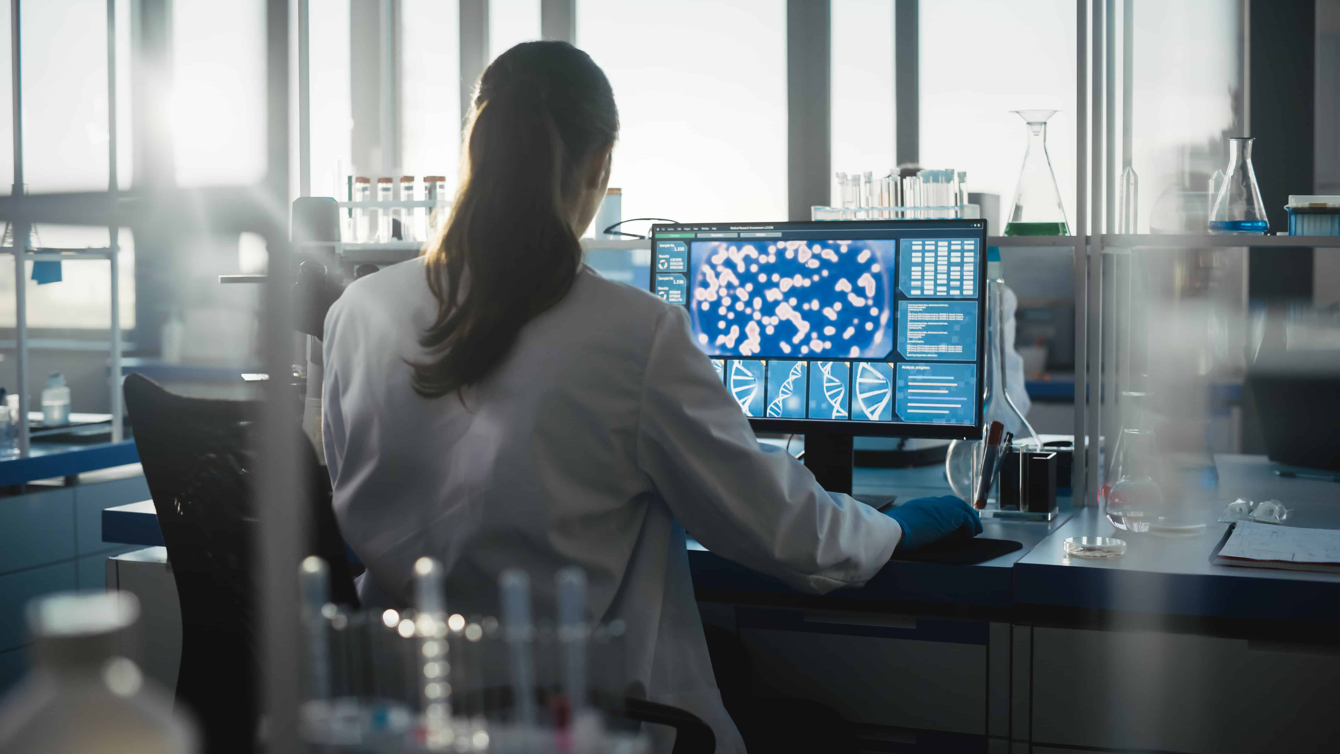 Medical Science Laboratory with Diverse Team of Professional Biotechnology Scientists Developing Drugs, Female Biochemist Working on Computer Showing Gene Therapy Interface